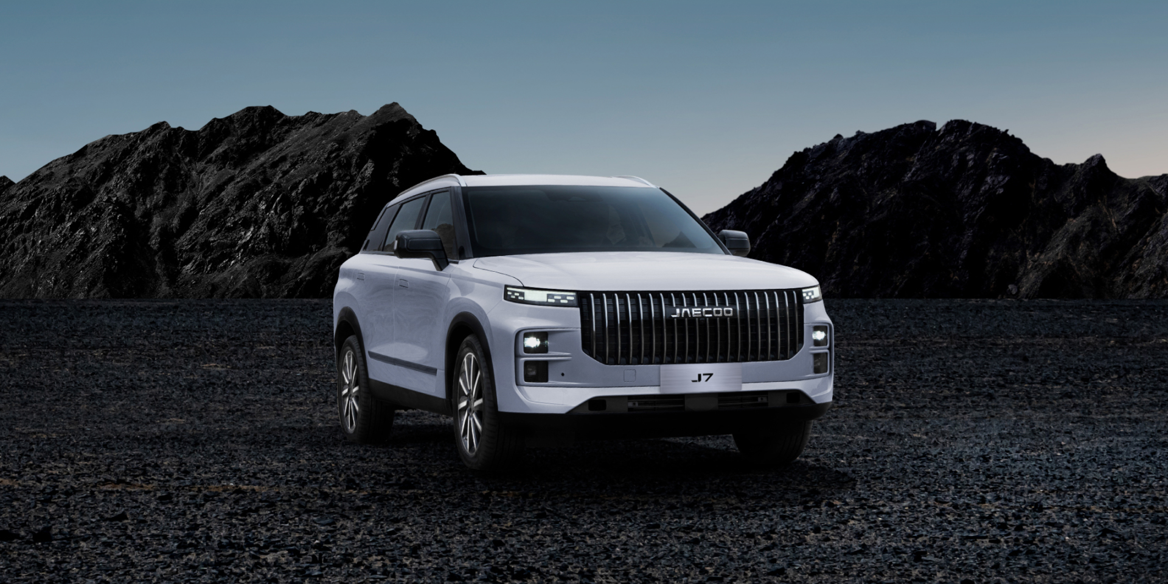 A new premium off-road SUV, the white JAECOO, is parked on a rocky terrain with dark mountains in the background under a cloudy sky, showcasing its JAECOO premium off-road performance.